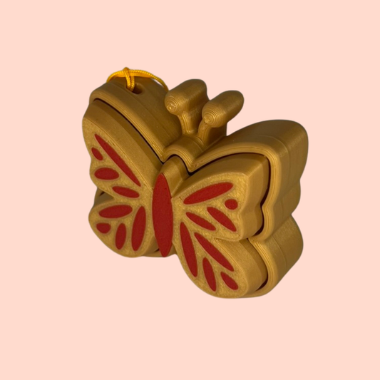 Gold butterfly-shaped object with red center on a pink background