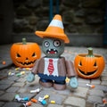 Toy figure in a candy corn hat with pumpkins and candy on a stone surface